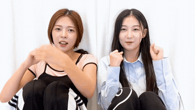 Two Young Women Are Sitting Next To Each Other With Their Fists In The Air . GIF