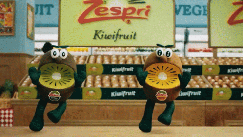Two Zespri Kiwifruit Characters Are Dancing In Front Of A Sign For Kiwifruit GIF