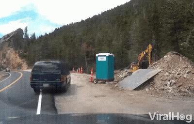 Van Driving Down Road Beside Portable Toilet And Bulldozer GIF
