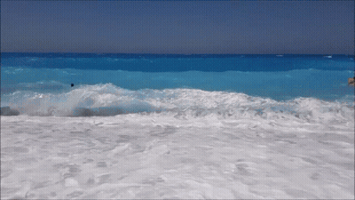 Waves Crashing Against A Sandy Beach With A Person In The Water GIF