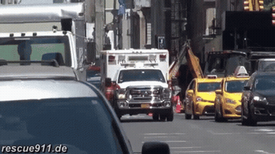 White Ambulance Driving Down Busy Street Next To Taxis GIF