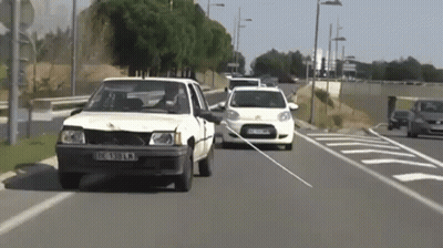 White Car With License Plate IC 389 KM Driving Down Street GIF