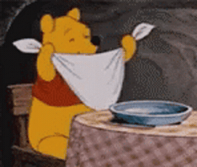 Winnie The Pooh Is Sitting At A Table Holding A White Towel Over His Head . GIF