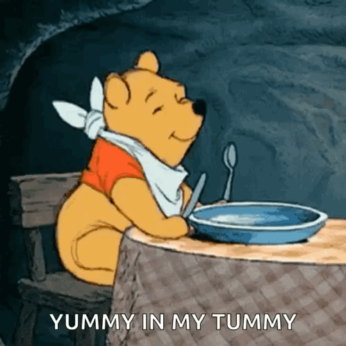 Winnie The Pooh Is Sitting At A Table With A Plate Of Food And A Spoon . GIF