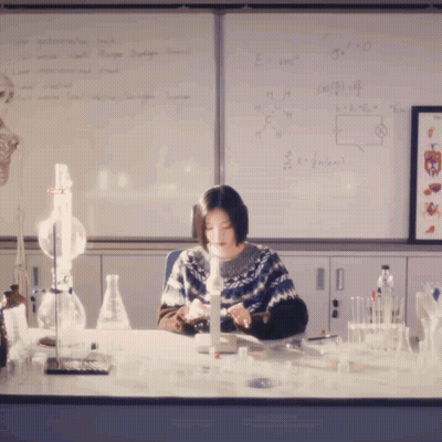 Woman At Desk With Equations On Whiteboard GIF