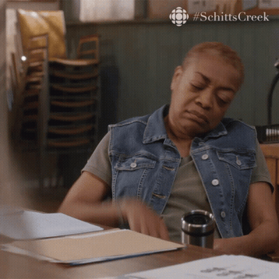 Woman At Desk With Stack Of Chairs Schitts Creek GIF