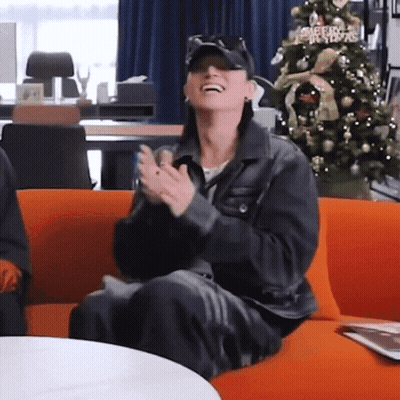 Woman Clapping On Orange Couch By Christmas Tree GIF