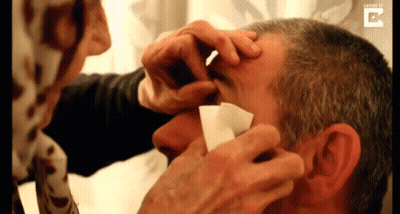 Woman Cleaning Man's Eye With Paper GIF