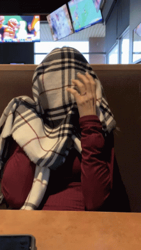 Woman Covering Face With Plaid Scarf In Restaurant GIF
