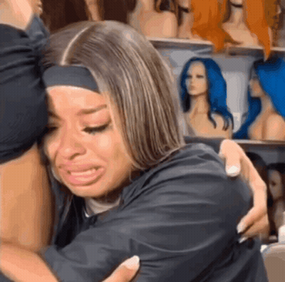 Woman Crying Hugging Another Woman In Front Of Wigs GIF