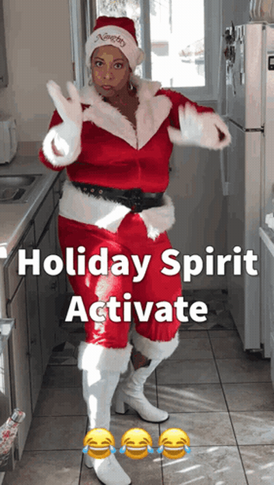 Woman Dressed As Santa Claus In Kitchen Saying Holiday Spirit Activate GIF