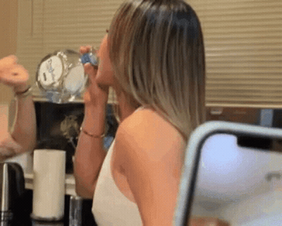 Woman Drinking Water From Bottle Looking At Phone In Mirror GIF