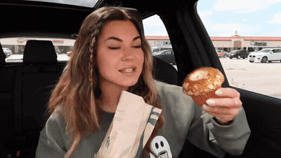 Woman Eating Muffin In Car With Big O's Background GIF