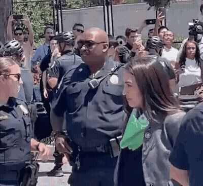 Woman Escorted By Police Officer As Crowd Takes Pictures GIF