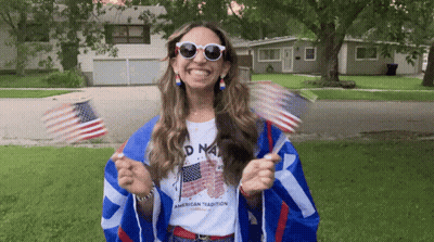 Woman Holding American Flags In American Tradition Shirt GIF