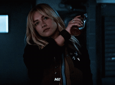 Woman Holding Bottle Saying Hi In Dark Room GIF