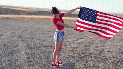 Woman Holding Large American Flag In Dirt GIF