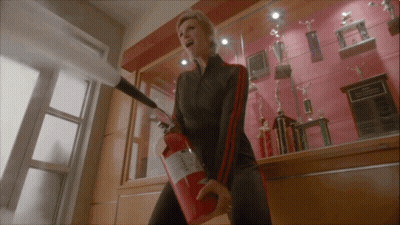 Woman Holding Red Fire Extinguisher In Front Of Trophies GIF