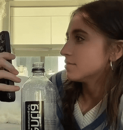 Woman Holding Remote Next To Bottle Of Bjing GIF