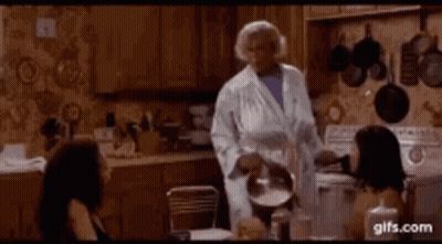 Woman In Bathrobe Holding Pot In Kitchen GIF