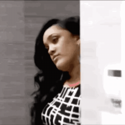 Woman In Black And White Dress Peeking From Behind Glass Door GIF