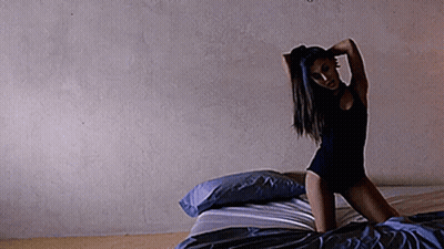 Woman In Black Bodysuit Kneeling On Blue Pillows GIF