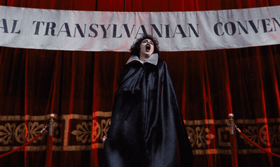 Woman In Black Cape In Front Of Transylvanian Convention Banner GIF