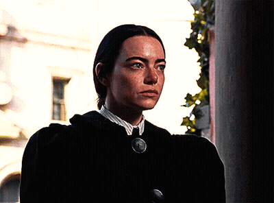 Woman In Black Coat And White Shirt With Medallion Necklace GIF