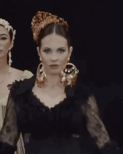Woman In Black Dress And Earrings Next To Crowned Woman GIF