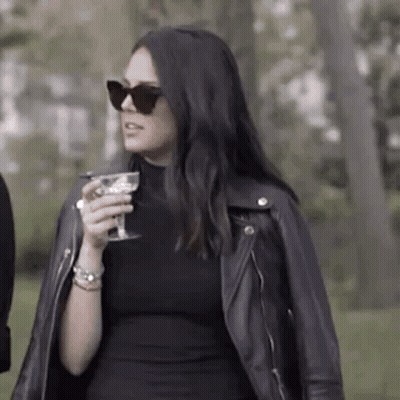 Woman In Black Dress And Leather Jacket Holding Wine GIF