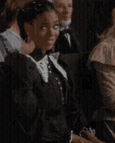 Woman In Black Dress And White Collar Smiling In Crowd GIF