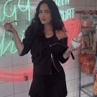 Woman in Black Dress Holding Ice Cream in Front of Yogurt Sign