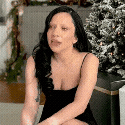 Woman In Black Dress Making Funny Face By Christmas Tree GIF