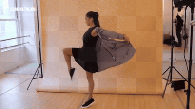Woman In Black Dress On One Leg Yellow Wall GIF