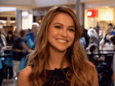 Woman In Black Dress Smiling In Crowded Mall GIF