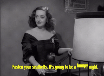 Woman In Black Dress Standing Next To Lamp Says Fasten Your Seatbelts GIF