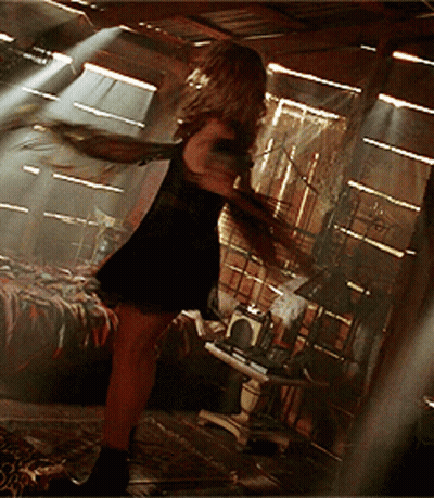 Woman In Black Dress With Arms Outstretched In Dark Room GIF