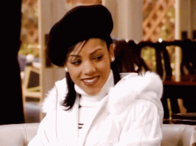 Woman In Black Hat And White Coat Smiles GIF
