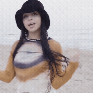 Woman In Black Hat And Yellow Shirt Standing On Beach GIF