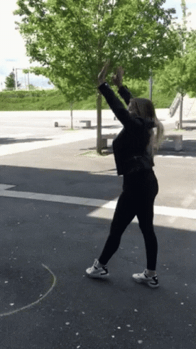 Woman In Black Jacket Arms In Air On Street GIF