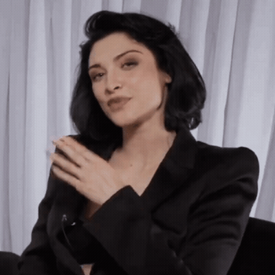 Woman In Black Jacket Sitting In Front Of White Curtain GIF
