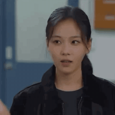 Woman In Black Jacket Standing In Front Of Door Looking At Camera GIF