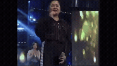 Woman In Black Jumpsuit Holding Microphone On Stage GIF