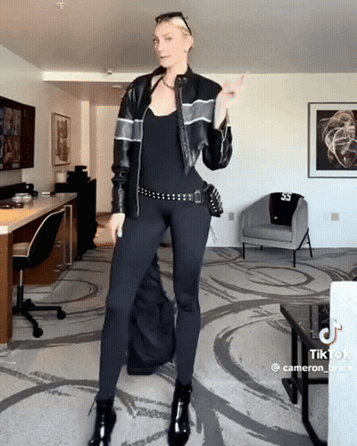 Woman In Black Leather Jacket And Leggings Standing In Living Room GIF