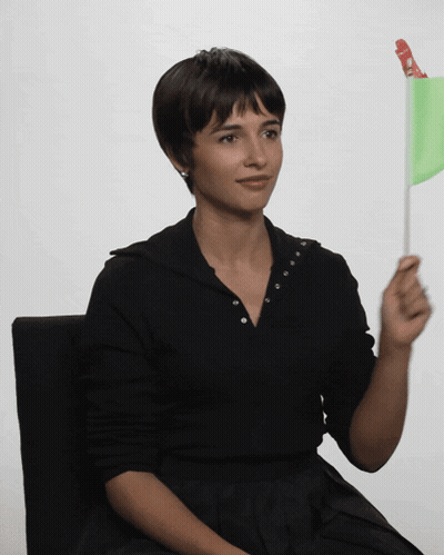Woman In Black Shirt Holding Green Flag With Red Circle GIF