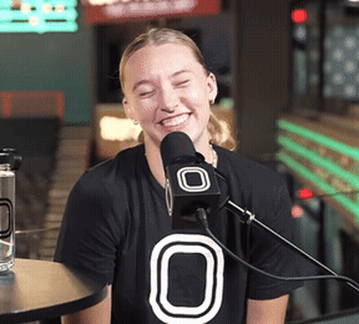 Woman In Black Shirt With O Smiling At Microphone GIF