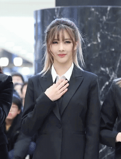 Woman In Black Suit Holding Hand To Heart GIF
