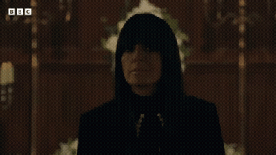 Woman In Black Suit Standing Before Cross In Dark Room GIF