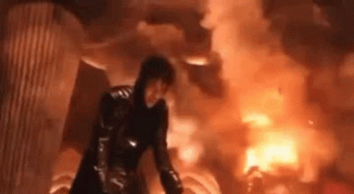 Woman In Black Suit Standing In Front Of Large Fire GIF