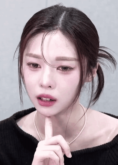 Woman In Black Sweater And Pearl Necklace Touching Chin GIF